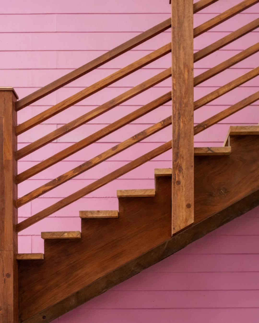 A timber staircase with a slatted balustrade rising across a pink clapboard wall